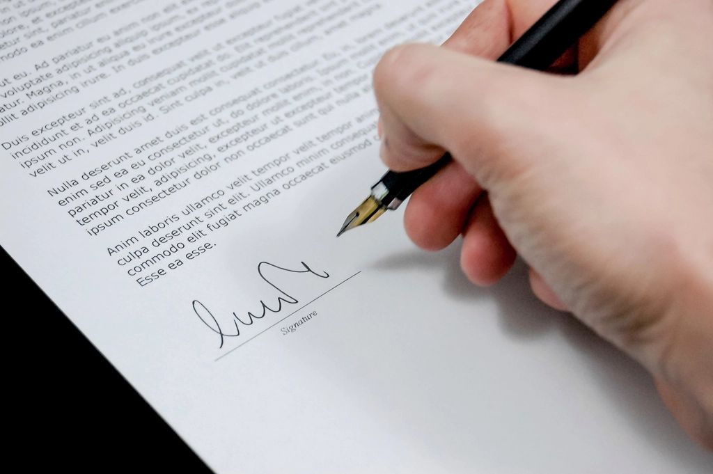 A hand signing a document with a pen